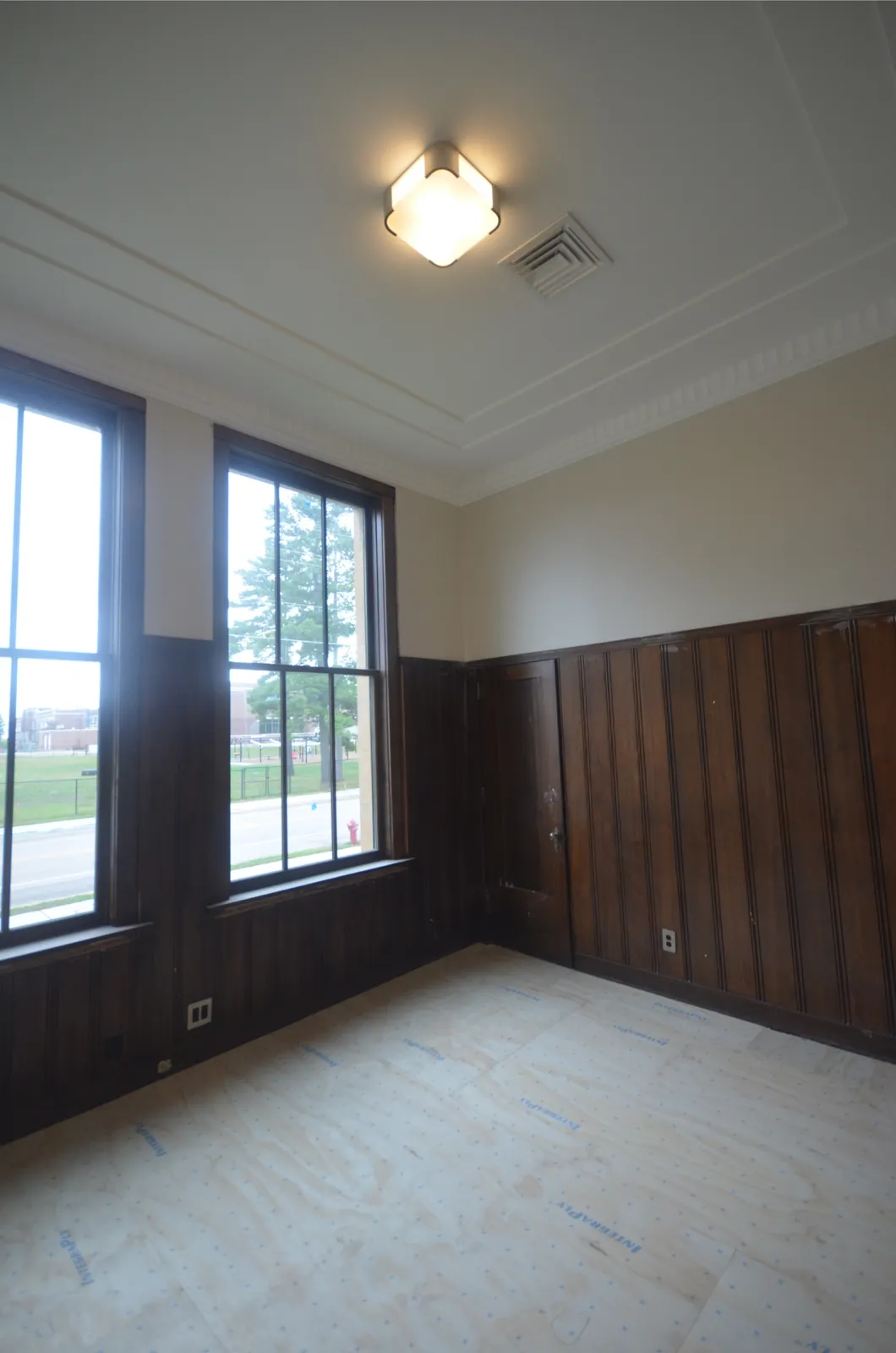 A private office with original dark wood wainscoting, tall windows and a new light fixture