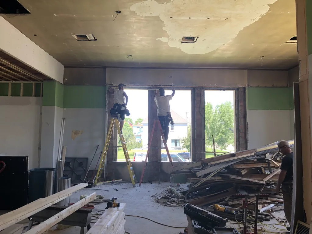 Carpenters on ladders at the tall window openings, seen from inside