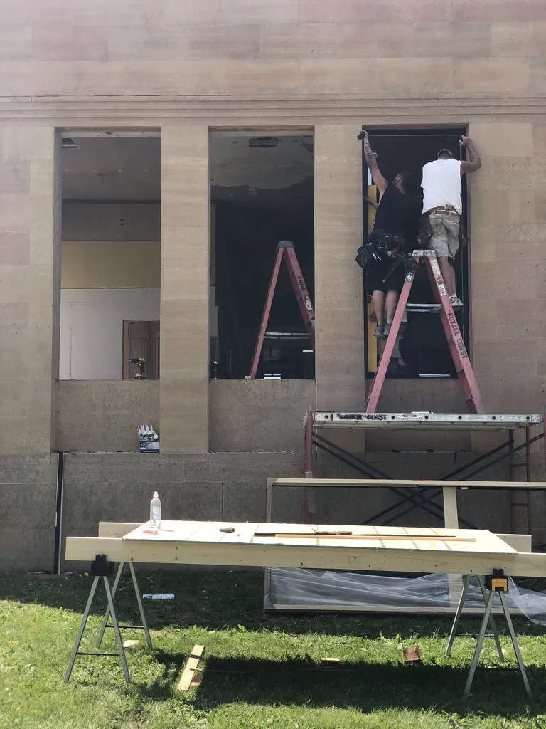 Workers on ladders setting new windows in the stone facade