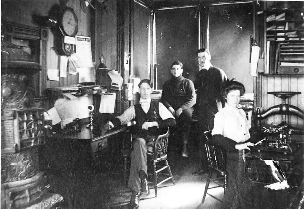 The depot office in 1909 with a pot-bellied stove, wall clock and four staff