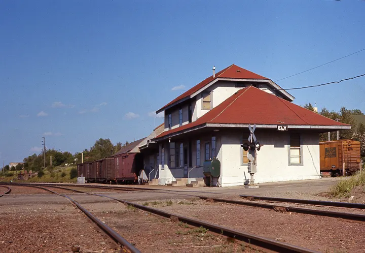 The depot with cream stucco walls and a red roof beside the tracks