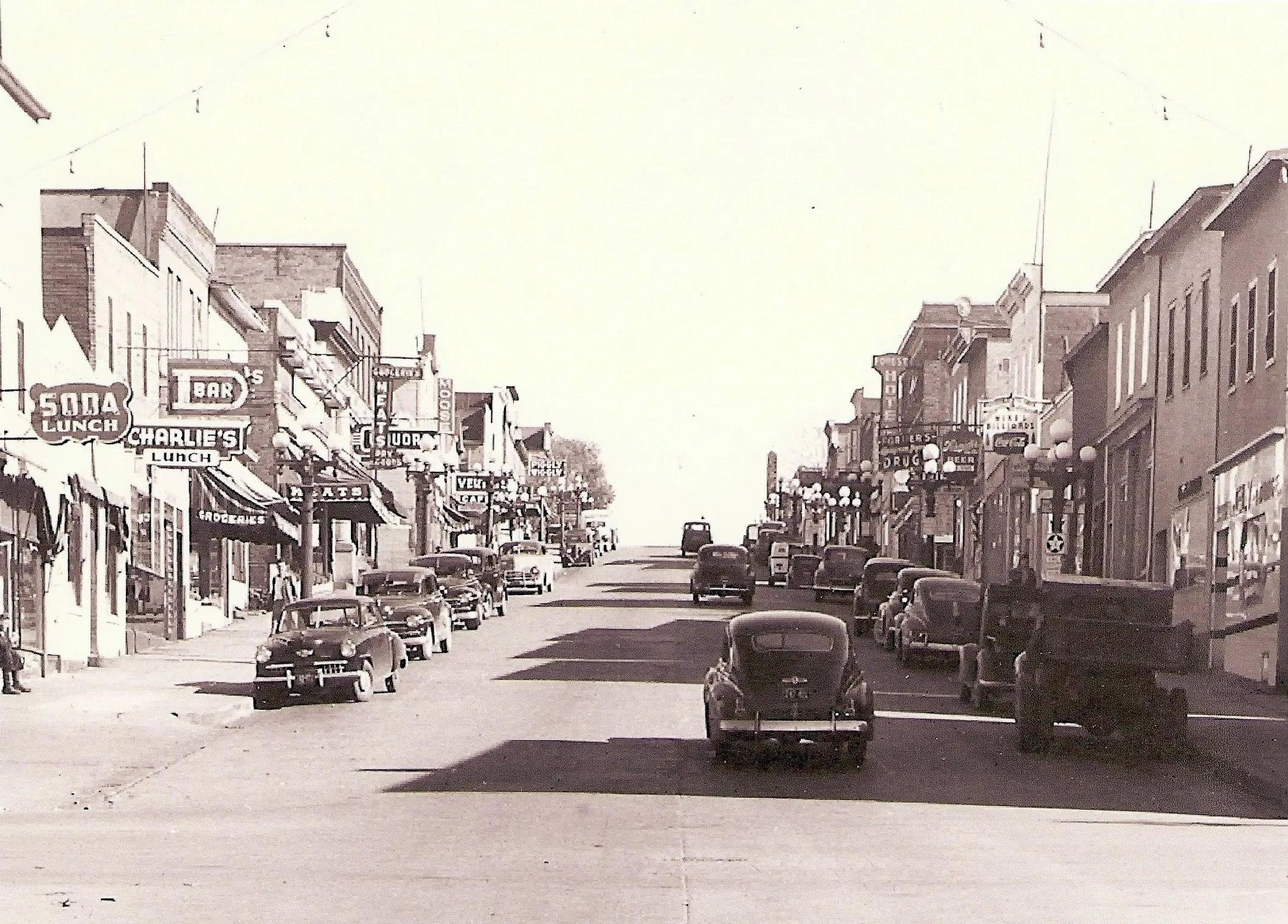 Sheridan Street in the 1940s lined with cars and signs for soda, lunch, meats and drugs
