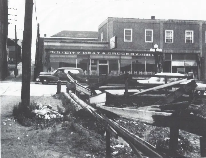 City Meat and Grocery storefront beside a two-story building, with mid-century cars