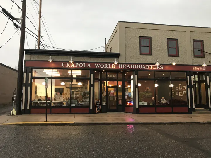 Crapola World Headquarters storefront glowing at dusk