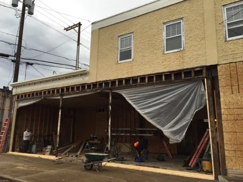 The one-story storefront opened up to its framing, with plastic sheeting and a wheelbarrow