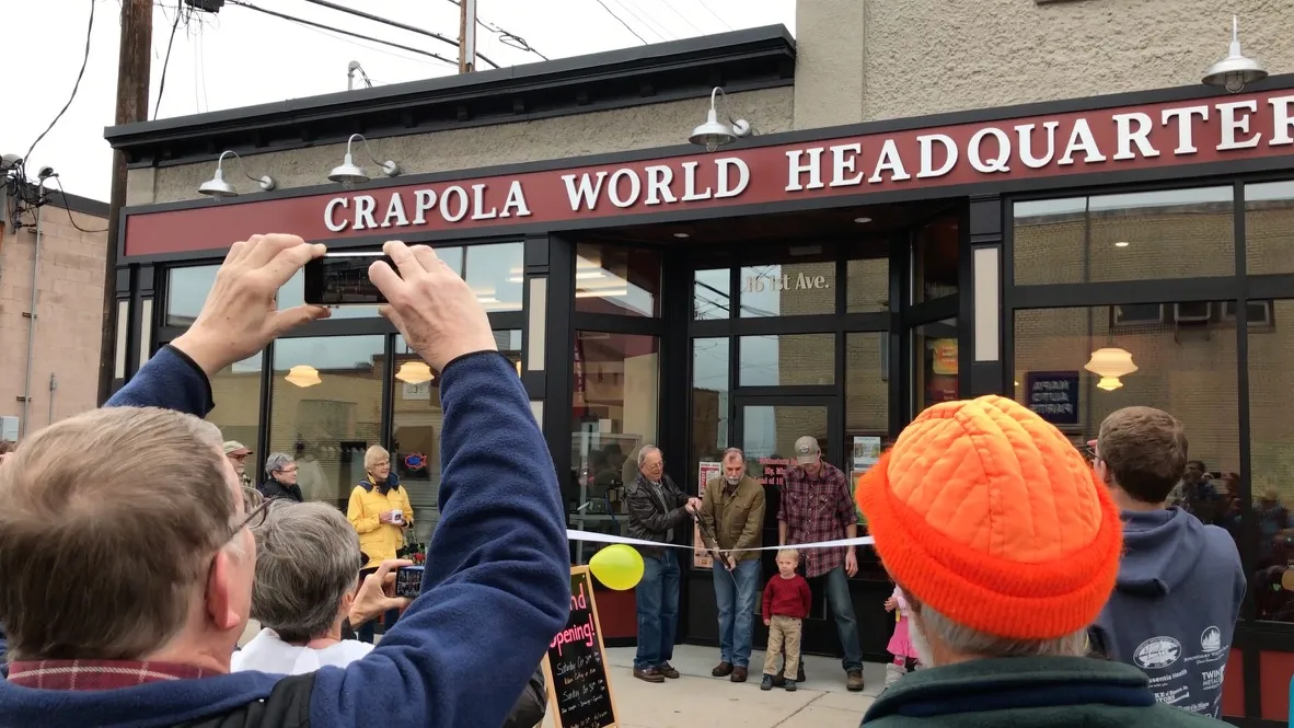 A crowd watching a ribbon cutting in front of Crapola World Headquarters