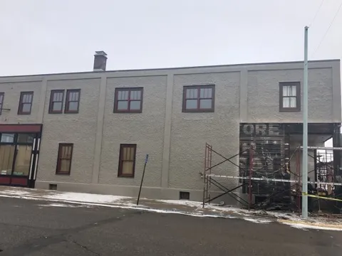 The stucco side of the building with new red-trimmed windows and scaffolding at the corner