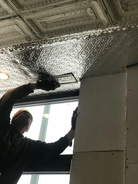 A worker fitting pressed tin ceiling panels above a new window