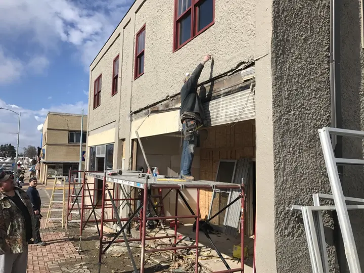A worker on scaffolding removing old facade material above a storefront