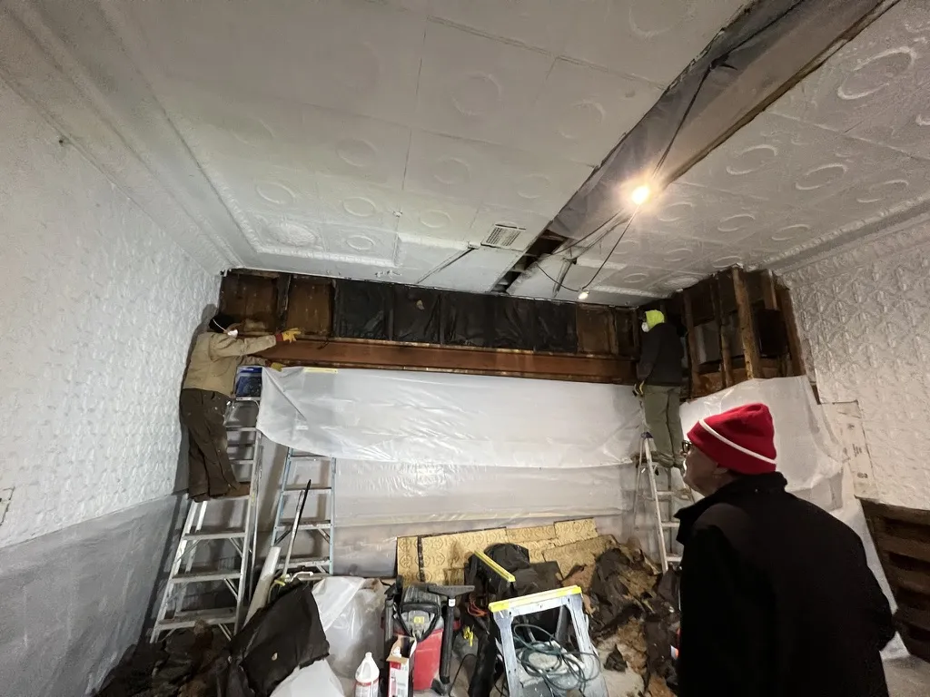 Workers on ladders exposing an old beam along the ceiling