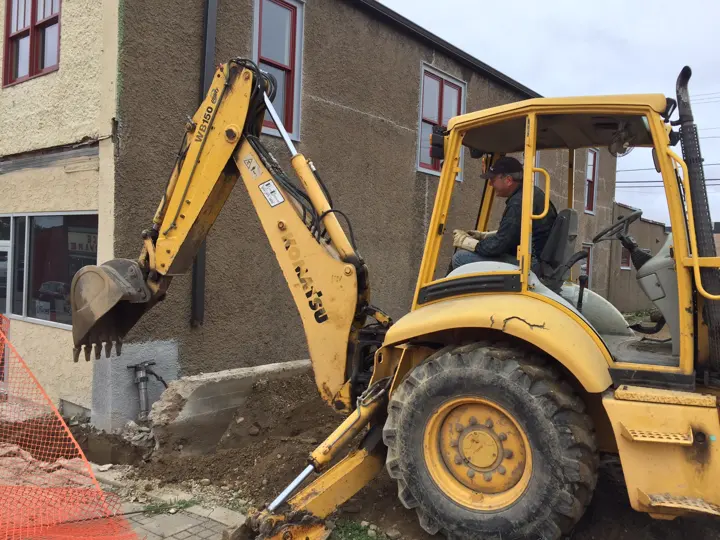 A backhoe breaking out an old concrete foundation beside the neighboring building