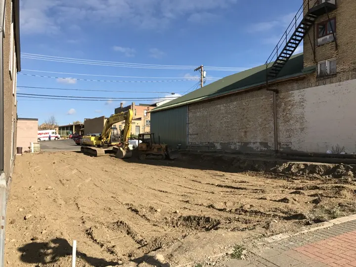 An excavator and bulldozer grading the empty lot between two buildings