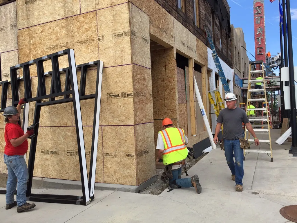 Crew installing black storefront window frames with the State sign behind