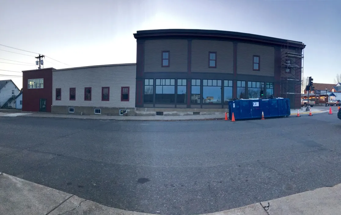 The new facade with a wall of storefront windows, scaffolding at the corner and a dumpster
