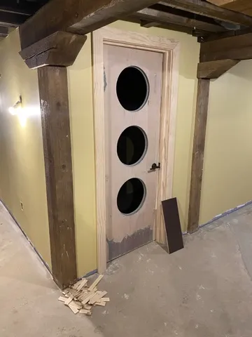 A pale wood door with three round porthole windows between timber posts on the lower level