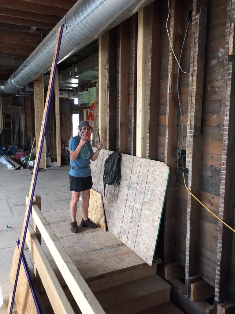 A worker holding a pry bar beside old wall framing