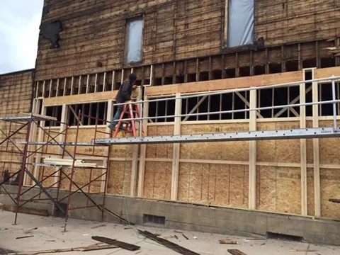 A worker on a ladder framing new storefront openings
