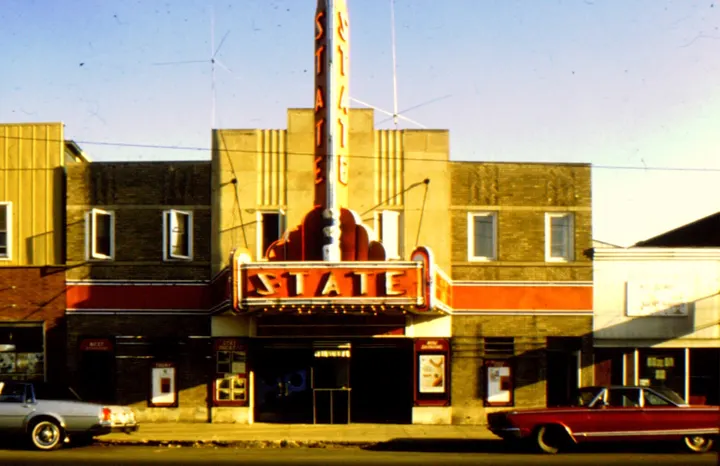 The State Theater in color with its red and yellow neon sign and marquee, with a 1970s car parked out front