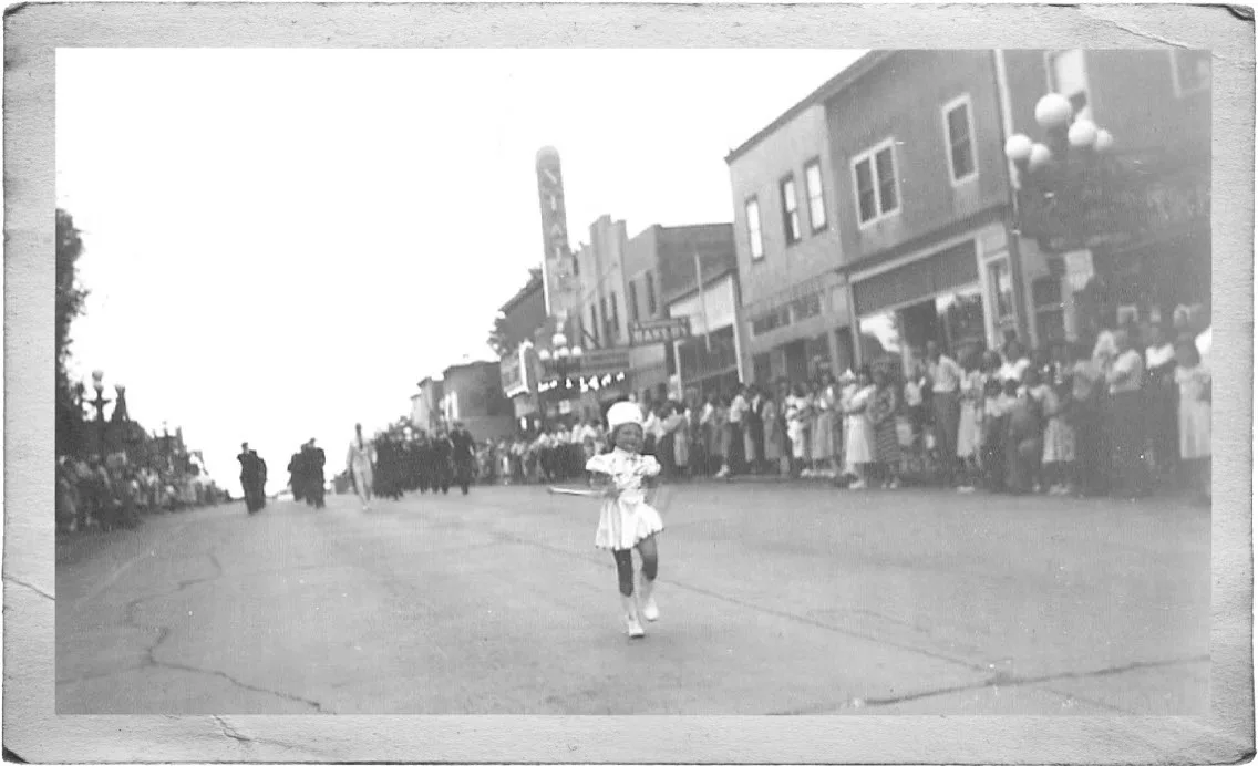 A young majorette leads a parade down Sheridan Street with the State Theater sign in the background