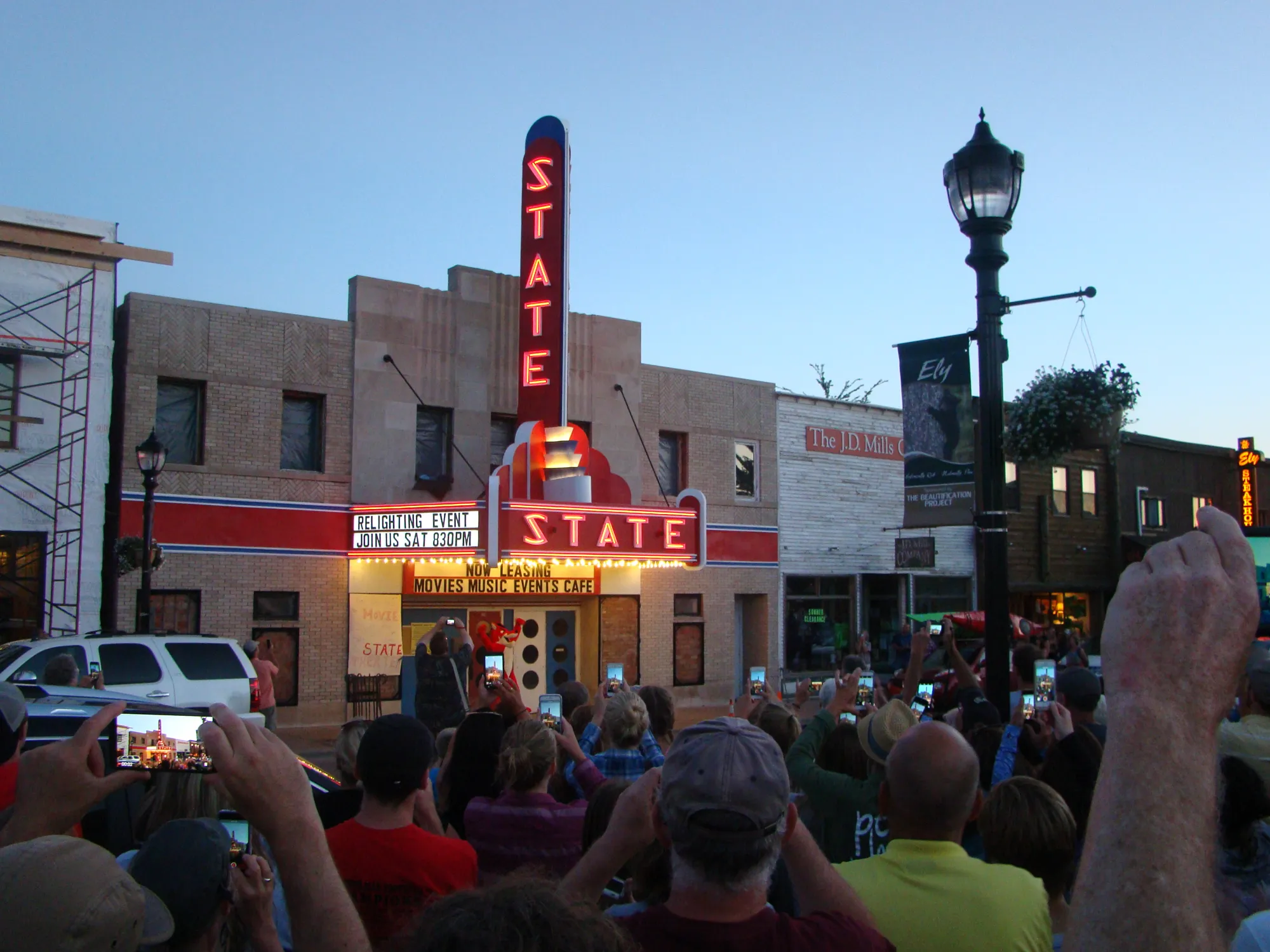 A crowd holding up phones as the State Theater's neon sign and marquee light up at dusk