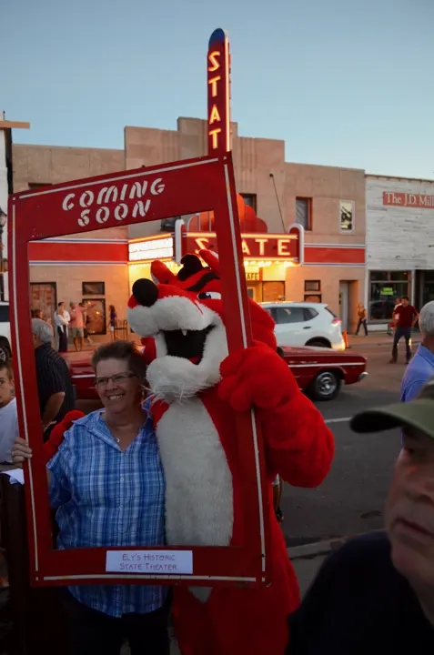 A guest and the mascot posing in a Coming Soon frame in front of the glowing theater