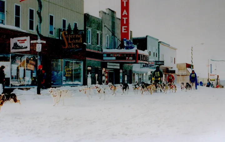 Sled dog teams racing down a snowy Sheridan Street past the State Theater