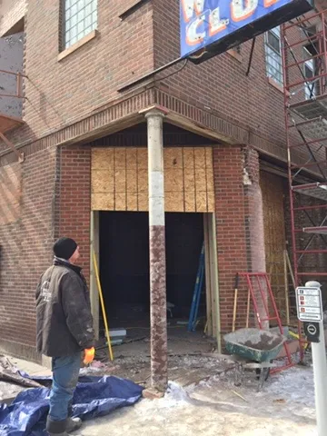 A worker looking up at a new corner entry opening under the old club sign